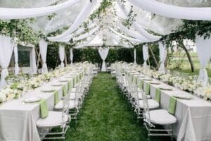 Elegant outdoor private event setup with long banquet tables under a white canopy, decorated for a formal garden event.
